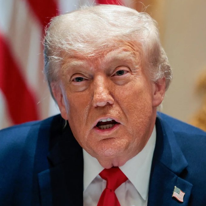Donald Trump, wearing a blue suit and red tie, is pictured speaking while an American flag pin is visible on his lapel. This image likely depicts him in relation to discussions about the crypto CLARITY Act.