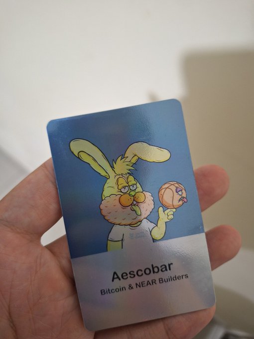 A hand holding a card featuring a cartoon rabbit character, labeled 'Aescobar - Bitcoin & NEAR Builders'.