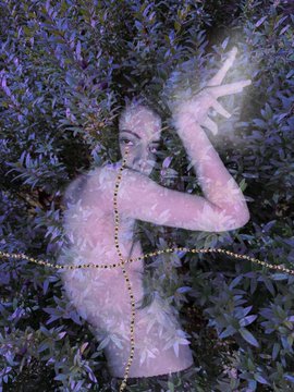 A surreal double-exposure style artwork of a person with raised hands blended into a background of foliage, decorated with small golden beads forming a pattern.