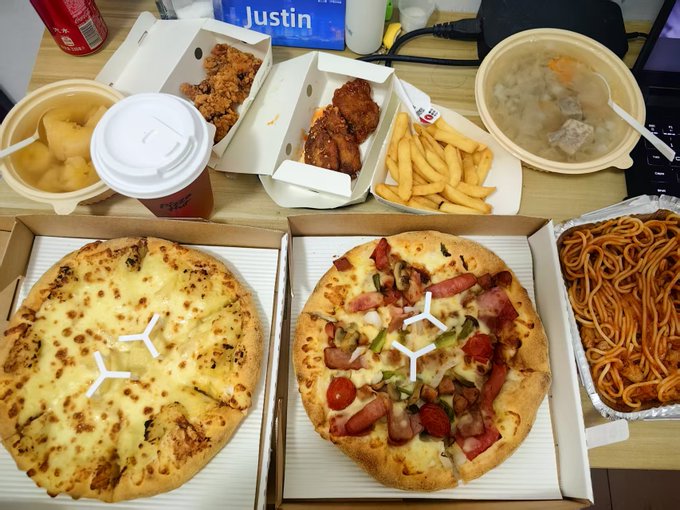 The image shows a dining table with two pizzas, one of which has a large amount of toppings such as pepperoni, sausage, and cheese. There are also other food items like noodles and a bowl of soup on the table. The table is covered in white paper plates, suggesting that it's set up for a meal or gathering. A cup can be seen near the center of the table, possibly containing a beverage to accompany the meal. The image seems to be related to Mike just eating today:HTX Pizza Fest' s pizza! Thanks @HuobiGlobal Usually, moving hundreds of U on-chain results in massive losses every time Who knows !!!