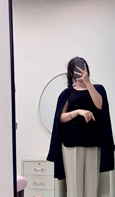 The image shows a woman taking a mirror selfie in a black cape-style top and light-colored pants. There's no visible text, numbers, or tickers in the image, so the caption doesn't need to include any. The post discusses the creator's growing viewership on content related to Injective, but the image itself simply depicts the person behind the account—a minimalist mirror selfie that pairs with the reflective theme of recounting their personal growth milestones.
