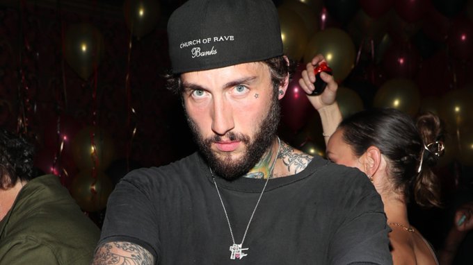 The image features a man wearing a black baseball cap with white text that says "Church of Rave". He has tattoos on his arms, and he's standing next to a group of people who are also wearing hats. The background includes balloons, which suggests that they might be at an event or party.