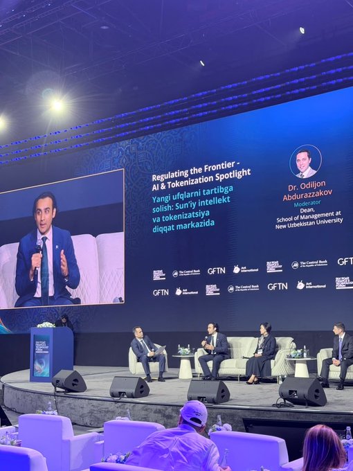 A panel discussion titled "Regulating the Frontier - AI & Tokenization Spotlight" features Dr. Odiljon Abdurazzakov, Dean of the School of Management at New Uzbekistan University, as moderator, alongside speakers including Bilal Bin Saqib (MoS) at the Silk Road Finance & Technology Forum. The Uzbek tagline on screen reads "Yangi ufqlarni tartibga solish: Sun'iy intellekt va tokenizatsiya diqqat markazida," while a speaker is shown on the large display screen addressing the audience seated on stage with microphones.