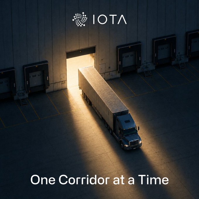 An aerial view of a semi-truck emerging from a warehouse at dusk with the 'IOTA' logo and tagline 'One Corridor at a Time.'