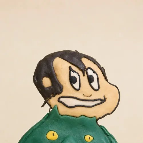 A decorated cookie shaped like a cartoon character's face with dark hair and a green jacket.