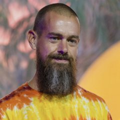 A bearded man with a shaved head wearing an orange and yellow tie-dye shirt.