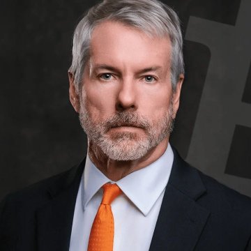 In the image, there's a man wearing a suit with an orange tie looking directly at the camera. The background of the photo is black and features the words "MicroStrategy" and "Bitcoin". The caption also includes information about Bitcoin trading and the addition of more Bitcoins to MicroStrategy's treasury. The main subject of the image is Michael Saylor, which may or may not be related to his suit.