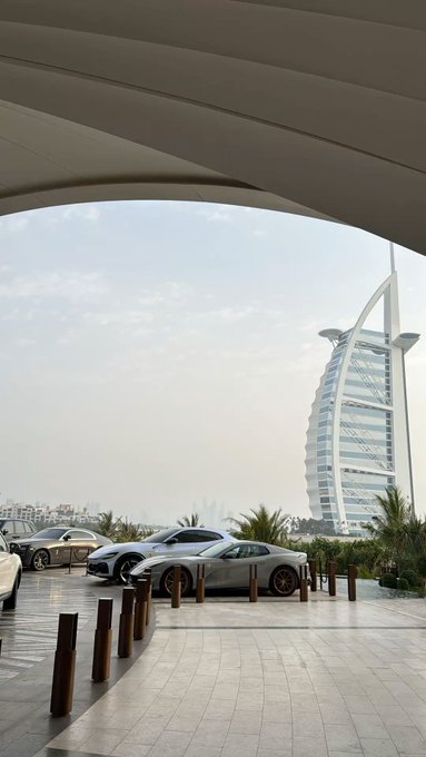 A sleek silver Chevrolet Corvette and other luxury cars are displayed at an upscale venue with the iconic Burj Al Arab hotel visible in the background, showcasing GM's premium automotive lineup against Dubai's renowned skyline.