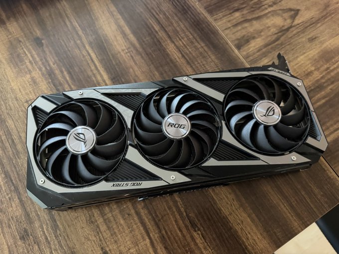 An ASUS ROG Strix graphics card with three cooling fans displayed on a wooden surface.