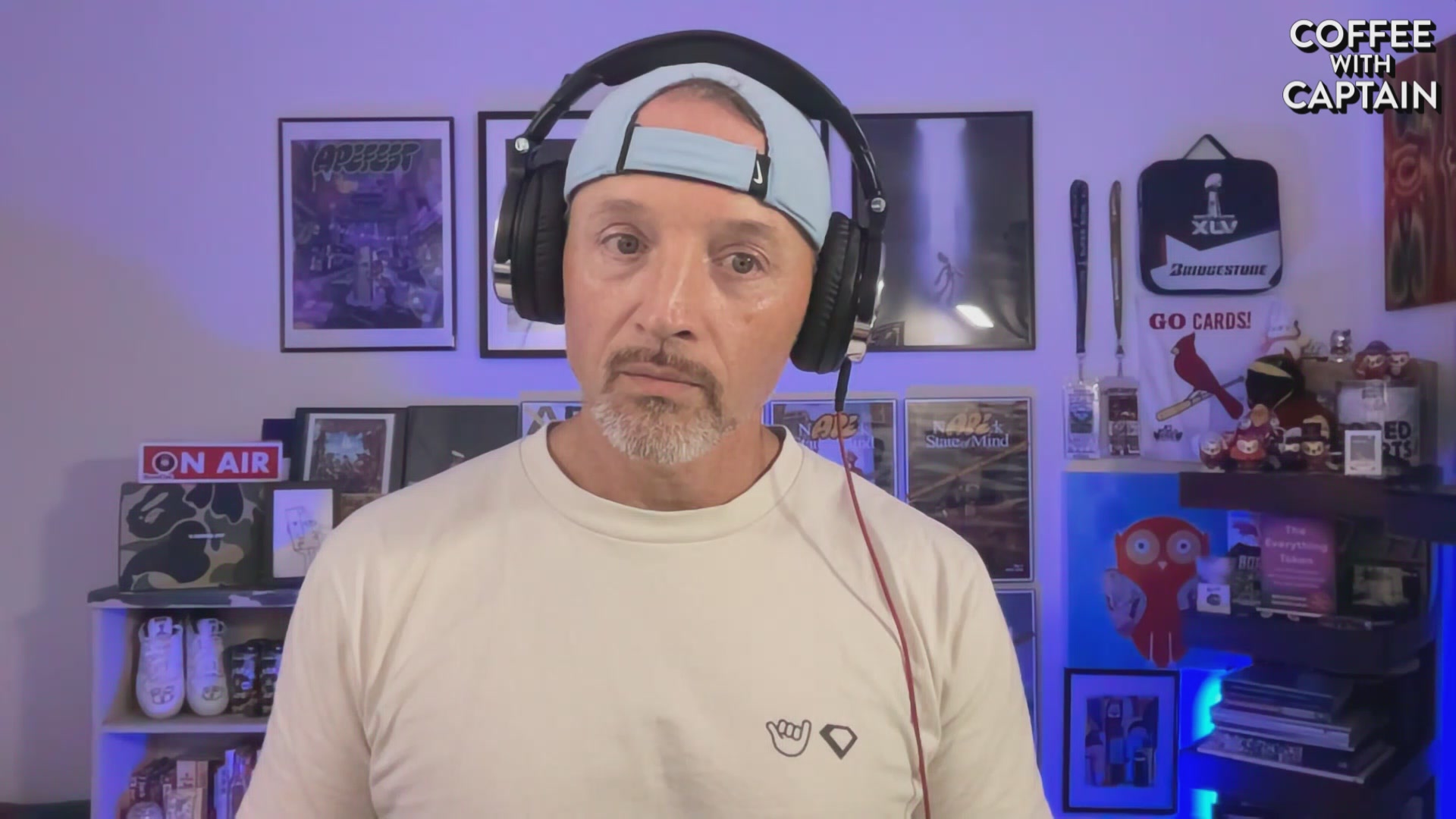 The image features a man wearing headphones and a white t-shirt who appears to be talking into a microphone or headset. The background of the image shows various posters and pictures hanging on the wall behind him. There are also several books scattered around, suggesting that he might have an interest in reading or studying. The post includes text that reads "Coffee with Captain #1,177" which could possibly be a reference to the creator of Coffee with Captain or another related project.