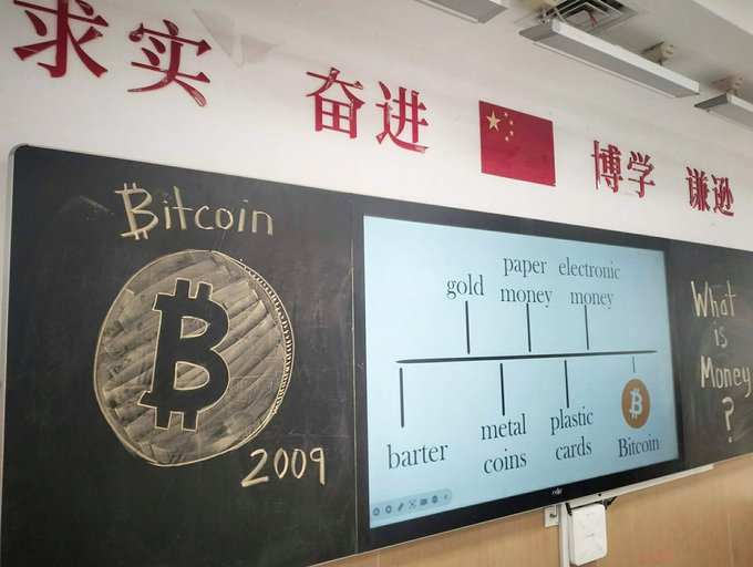A classroom blackboard displays a large Bitcoin logo with "2009" written below, alongside a digital screen showing the evolution of money: barter, metal coins, plastic cards, and Bitcoin, with Chinese characters above.