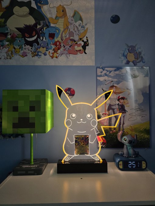 A Pokémon-themed room setup features a glowing Pikachu acrylic lamp, a Minecraft Creeper lamp, a Pokémon poster, and a small Mew figurine on a digital clock showing 25:1.