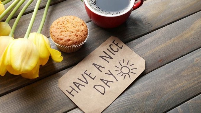 A muffin, yellow tulips, and a red mug of coffee sit on a wooden table next to a kraft tag reading "HAVE A NICE DAY ☀️," perfectly matching the "Good Morning" post's cheerful wish for a fresh, energizing new week.