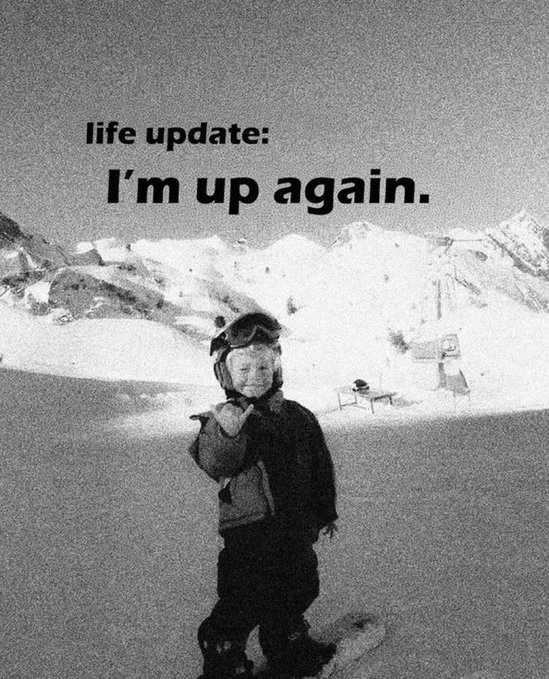 A black and white vintage-style photo of a young child wearing ski goggles on a snowboard with mountains in the background, overlaid with the text 'life update: I'm up again.'
