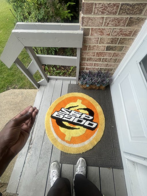 A person holds a "SPX 6900" branded rug in their hand while standing on a porch next to its matching doormat, with the same logo displayed on both. This ties directly to the ongoing "Day 251" series promoting SPX6900, a meme coin parodying the S&P 500.