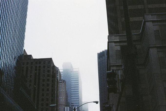 A moody, foggy urban street view with skyscrapers and traffic lights, shot on film.