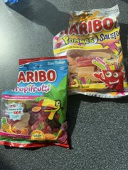Two bags of Haribo gummy candy, including 'Tropifrutti' and 'Yogurt Gums,' lying on a dark textured surface.