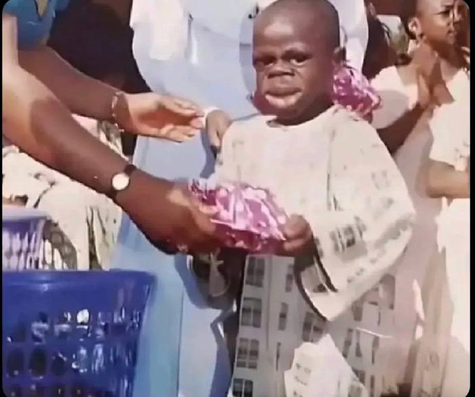 A heartwarming scene of a crying young child being handed a wrapped gift from someone in a blue outfit.