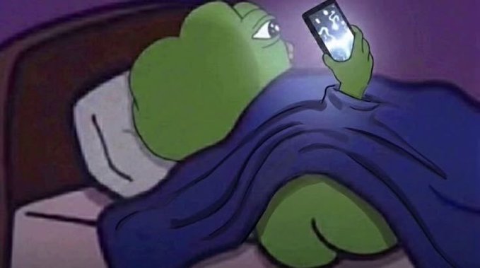 A green frog character lies in bed under a blue blanket, holding up a phone displaying "15" (likely a weather/temperature app) in a dimly lit room. The image pairs with the "gm" (good morning) post to humorously depict the relatable scene of waking up and immediately checking your phone.