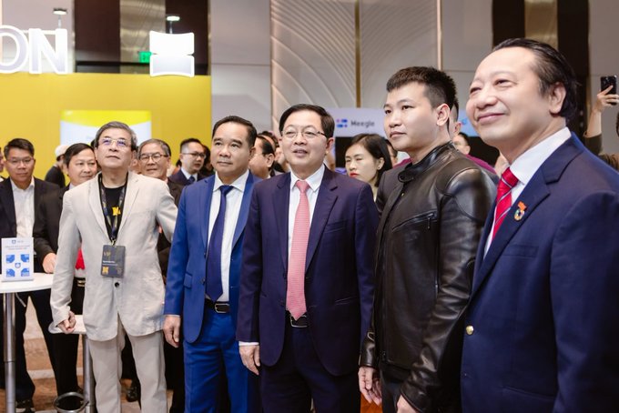 A group of formally dressed men in suits pose together at what appears to be a corporate event, with one in a black leather jacket.