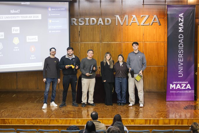 Six individuals stand on a wooden stage at Universidad Maza in Mendoza, holding awards in front of a presentation screen displaying the "Binance University Tour AR 2026" Kahoot leaderboard, with a purple Universidad Maza banner visible to the right.