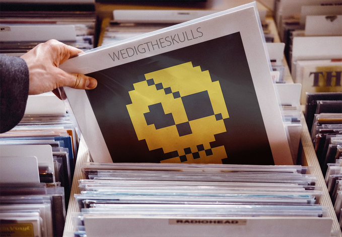 A hand holds up a vinyl record album titled "WEDI THE SKULLS" featuring a pixelated yellow skull design on a black cover, displayed in a record store bin above "RADIOHEAD" records.