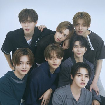 Seven young men pose closely together in a styled group portrait against a light background, wearing coordinated dark-toned outfits in shades of black, navy, and gray, with soft lighting highlighting their features. The composition reflects the polished, team-oriented aesthetic of K-pop promotional photography, fitting the hashtags #ALPHADRIVEONE #ALD1 #알파드라이브원, which likely promote the group's debut or a related project.