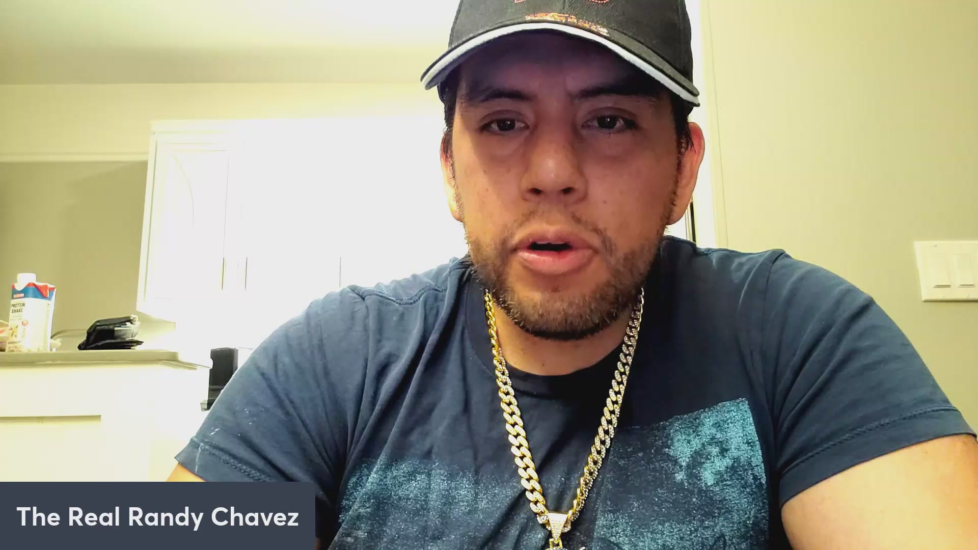 The image features a man wearing a black baseball cap with a gold chain around his neck. He has a serious expression as he looks directly at the camera. The caption of the image includes some text that reads "Why are people hyped about VeVe and $OMI?! VeeFriends, $DEFX Dacat Loki news!". This suggests that there is an ongoing discussion or trend related to the brand VeVe or a specific product involving the character $OMI.