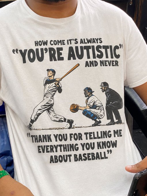 A person wears a white t-shirt featuring a vintage baseball illustration and text that reads: 'HOW COME IT'S ALWAYS "YOU'RE AUTISTIC" AND NEVER "THANK YOU FOR TELLING ME EVERYTHING YOU KNOW ABOUT BASEBALL"'.