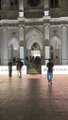 A blurry, low-resolution image showing what appears to be people walking through a large arched doorway or entrance to a building.
