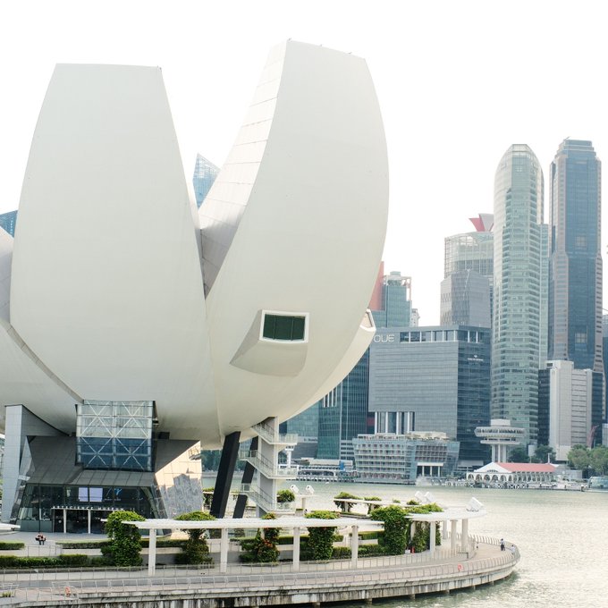 The image shows the ArtScience Museum, an iconic lotus-shaped building in Singapore, set against the city's financial district skyline with the "OUE" signage visible on a nearby building. This view of Singapore's Marina Bay area visually anchors the news about the Monetary Authority of Singapore's proposed stablecoin reserve requirements, highlighting the city-state's role as a major Asian financial hub tightening cryptocurrency oversight.