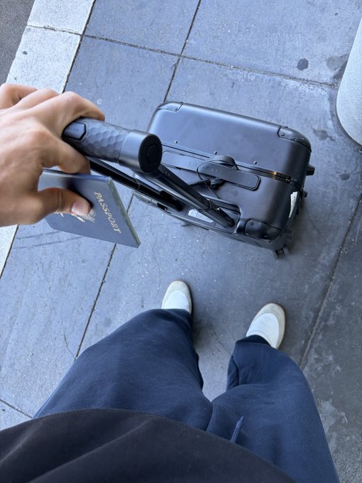 A traveler holding a US passport and a NEO-branded suitcase stands on a sidewalk, ready to board a flight to Japan to explore humanoid innovation and Japanese culture.