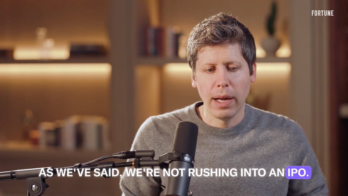 A man in a gray sweater speaks into a microphone in a softly lit room with bookshelves, with "FORTUNE" displayed in the top right corner and the caption "AS WE'VE SAID, WE'RE NOT RUSHING INTO AN IPO." appearing at the bottom. The image appears to be from a Fortune interview discussing IPO strategy, relating to the post's mention of catching market moves early through trading insights.