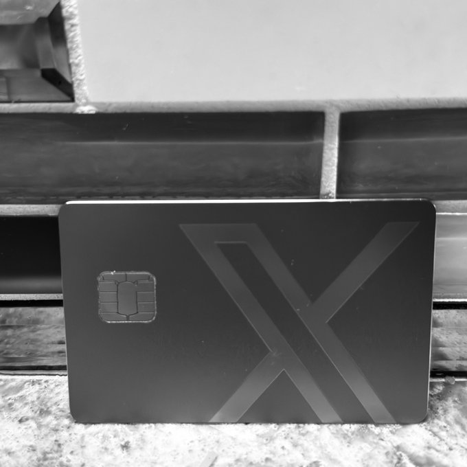 A black and white photo of a black card featuring a large "X" design and a smart chip, leaning against a wooden surface.