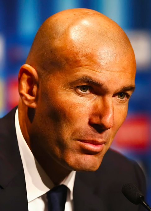 A bald man in a dark suit and navy tie sits at a press conference microphone with a serious, contemplative expression, his gaze directed off-camera. The accompanying post identifies him as Zinedine Zidane reflecting on his infamous headbutt of Materazzi during the 2006 World Cup final, his somber demeanor mirroring the reflective tone of his remarks.