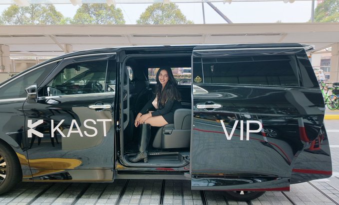 A woman sits in the open sliding door of a black van labeled “K KAST” and “VIP,” posing during a VIP ride to an event.