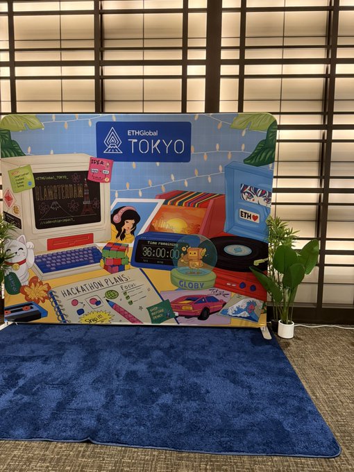 A colorful photo booth backdrop for ETHGlobal TOKYO featuring retro 80s/90s computer and synthesizer graphics, 'HACKATHON PLANS' sticker, a Lucky Cat figurine, plants, and a blue rug on the floor.