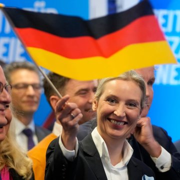 Alice Weidel, co-leader of Germany's AfD party, smiles while waving a German flag at a political event, celebrating the party's victory in the latest state election where they emerged as the largest party after campaigning on pro-Bitcoin policies including opposing CBDCs.
