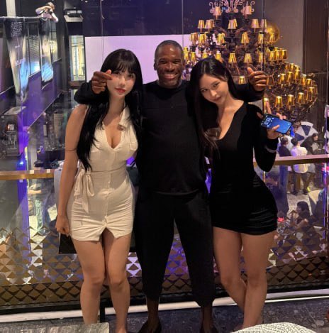 The image shows a man posing with two women at what appears to be an upscale nightclub, indicated by a "Substance" sign and chandeliers in the background. This relates to the post about Arthur Hayes, the BitMEX co-founder known for his lavish lifestyle, launching a new AI-related crypto protocol—evoking skepticism about the project's seriousness given his reputation for extravagant partying over technical substance.