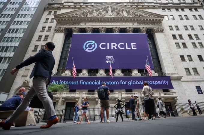 A banner reading "CIRCLE CRCL NYSE" with the slogan "An internet financial system for global prosperity" hangs above the New York Stock Exchange building, where pedestrians gather on the sidewalk outside.

The image relates to the post by showing Circle's recent market debut on the NYSE under ticker CRCL, the same listing now facing Wall Street scrutiny as analysts like Mizuho and JPMorgan turn cautious on the stock.