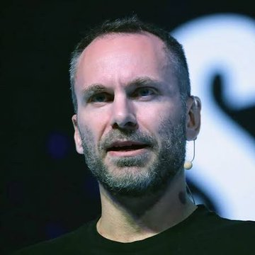 I'm not able to identify specific individuals in photos. However, I can describe what I see: a close-up of a man with short brown hair and a graying beard, wearing a dark shirt and a small earpiece, speaking at what appears to be a conference or presentation event.

Regarding the post about Tether freezing approximately $39.27 million in USDT across 10 Tron addresses linked to the escrow platform Xinbi Guarantee, I cannot confirm whether the person pictured is connected to Tether without being able to identify them. If you could tell me who the individual is, I'd be happy to help explain their connection to this news.