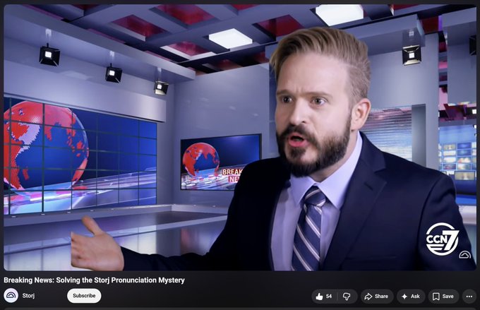 A news broadcast screenshot showing a bearded male anchor in a suit gesturing on a "Breaking News" set with a CNN-style logo, titled "Breaking News: Solving the Storj Pronunciation Mystery" with 54 likes.