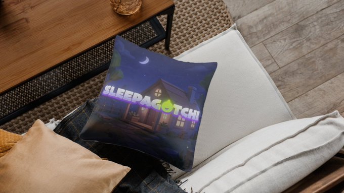 A decorative pillow featuring the 'SLEEPAGOTCHI' logo with a nighttime house illustration rests on a chair next to a wooden side table.
