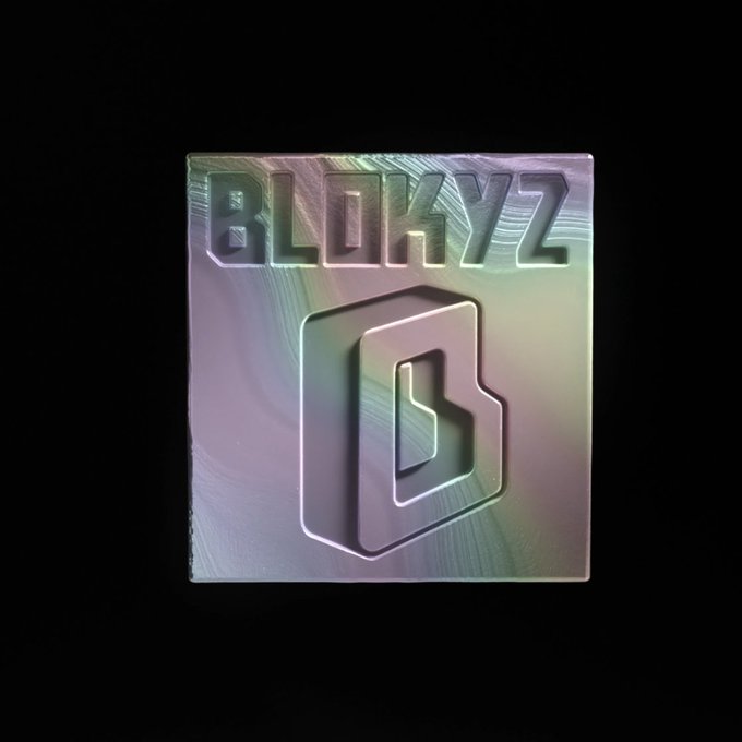 A holographic, iridescent logo featuring the word "BLOKZ" above a stylized "B" shield emblem, set against a black background.