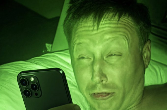 A man lies in bed, illuminated by the eerie green glow of his iPhone, squinting with a wide-eyed, shocked expression as he stares at the screen. The image humorously captures the caption's scenario of a sleep-deprived Bitcoin holder jolted awake by BTC soaring past $72,000.