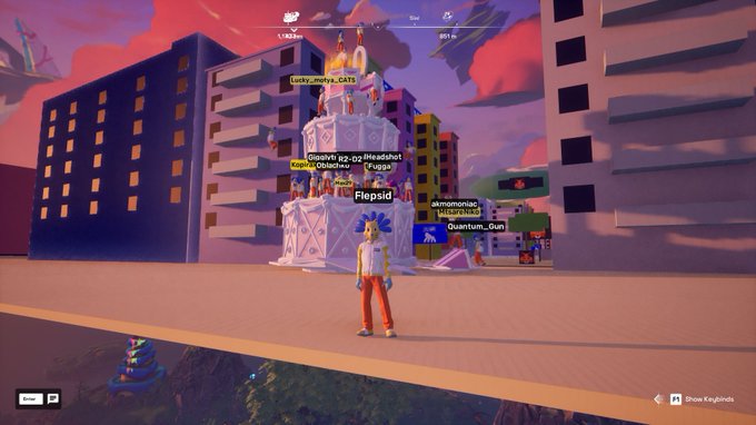A screenshot from a video game showing a character with blue hair standing in front of a large, multi-tiered white structure in a city setting, with other players' names floating above.