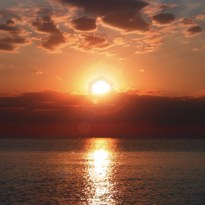 A glowing sunset over the ocean, with the sun's reflection shimmering across the water beneath a dramatic, cloudy sky. The serene, transitional scene mirrors the post's message of patience, symbolizing a quiet moment before dawn amid $CORE's temporary downturn.