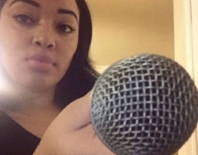 A selfie of a woman with dark hair holding a microphone near her face.