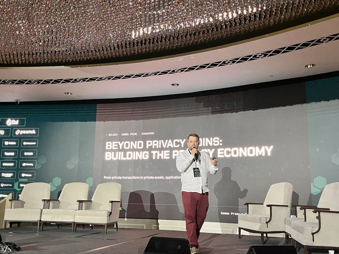 A man speaking on stage at a conference about "Beyond Privacy Coins: Building the Privacy Economy," discussing private transactions, with event partner logos visible on screen.