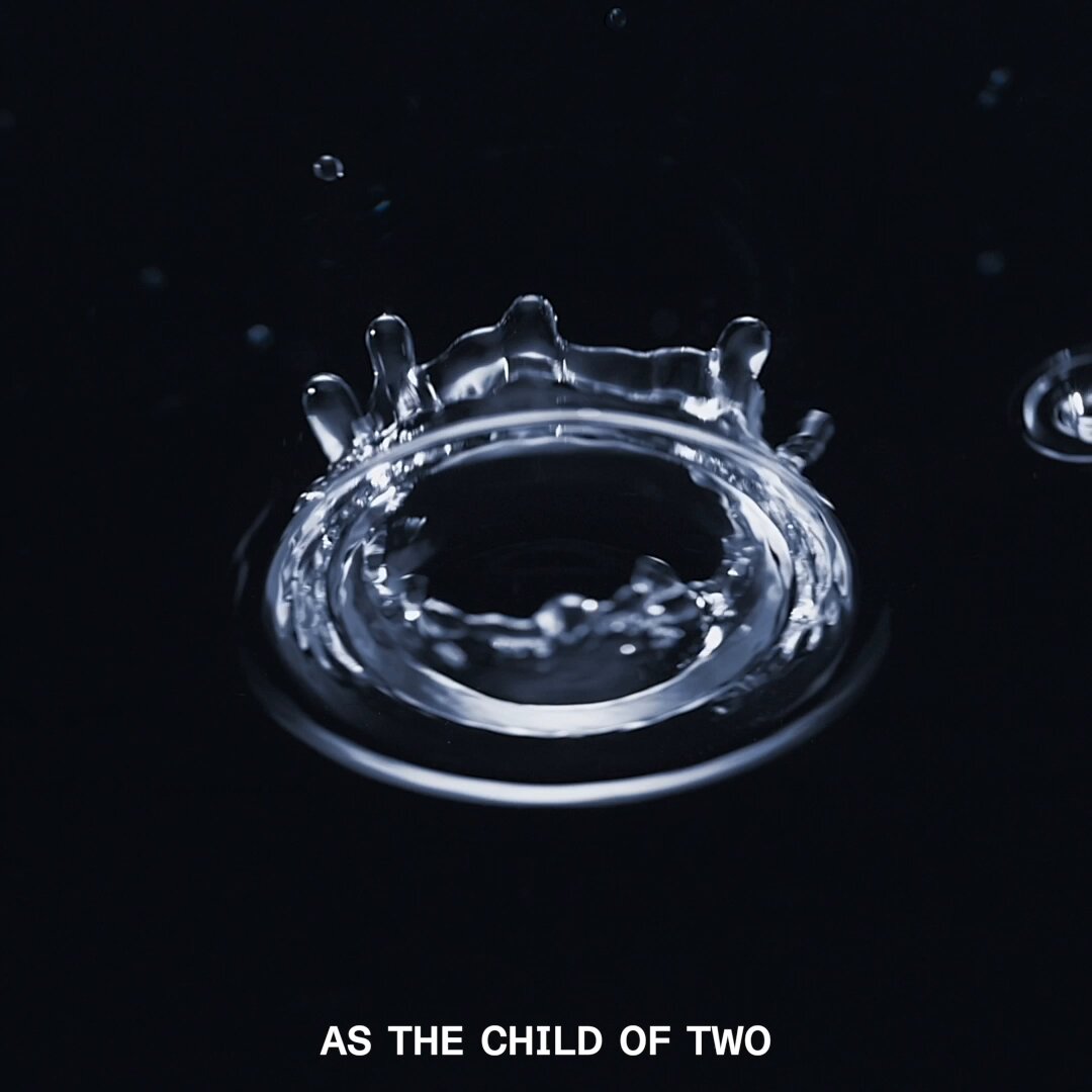 The image features a water droplet with a ring around it, which appears to be the center of attention. The background is black, making the water droplet stand out prominently. Below the image, there's text that reads "As the child of two". This phrase seems to be related to the water droplet and its ring-like shape, possibly suggesting a connection between the droplet and the concept of being the child of another person or an idea.